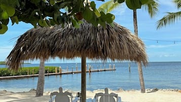 A beach with a thatched umbrella, white chairs, and a view of the ocean.
