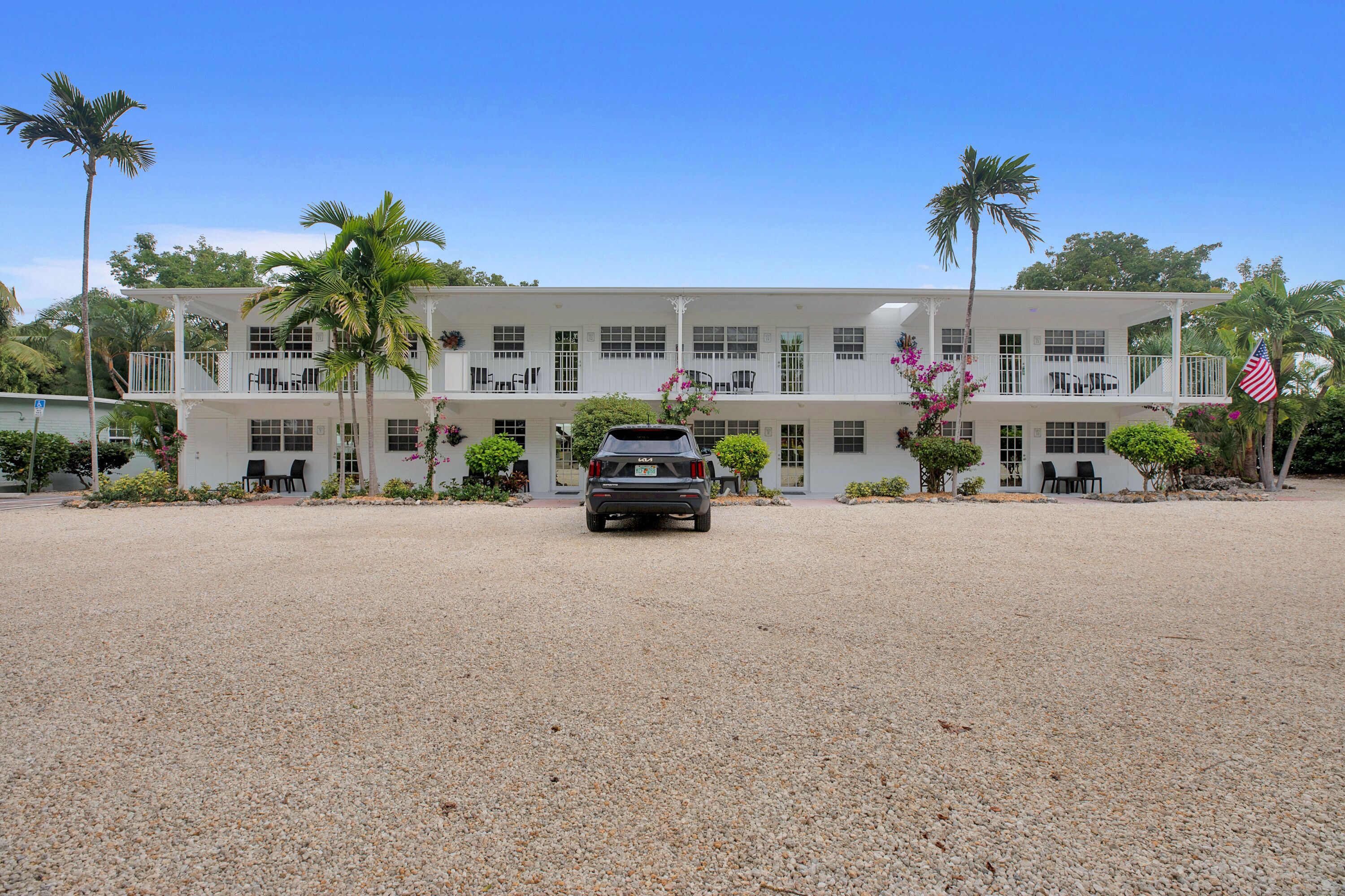A two-story white building with a gravel driveway and a parked car.