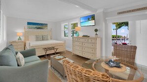 Une chambre spacieuse comprenant un lit, une commode, un téléviseur et une vue sur la mer par la fenêtre.