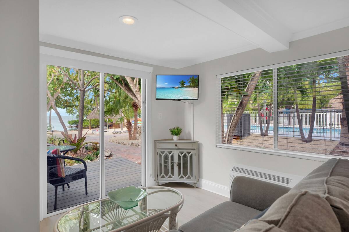 A living room with a glass table, a sofa, and a TV displaying a beach scene.