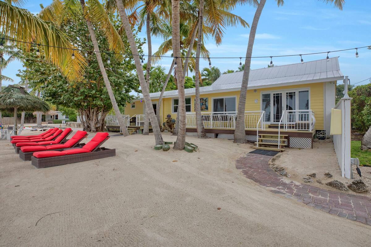 A beachside building with a yellow exterior, a covered patio area, and red lounge chairs.