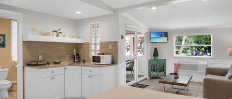 A modern kitchen with white cabinets, a microwave, and a window overlooking a balcony.