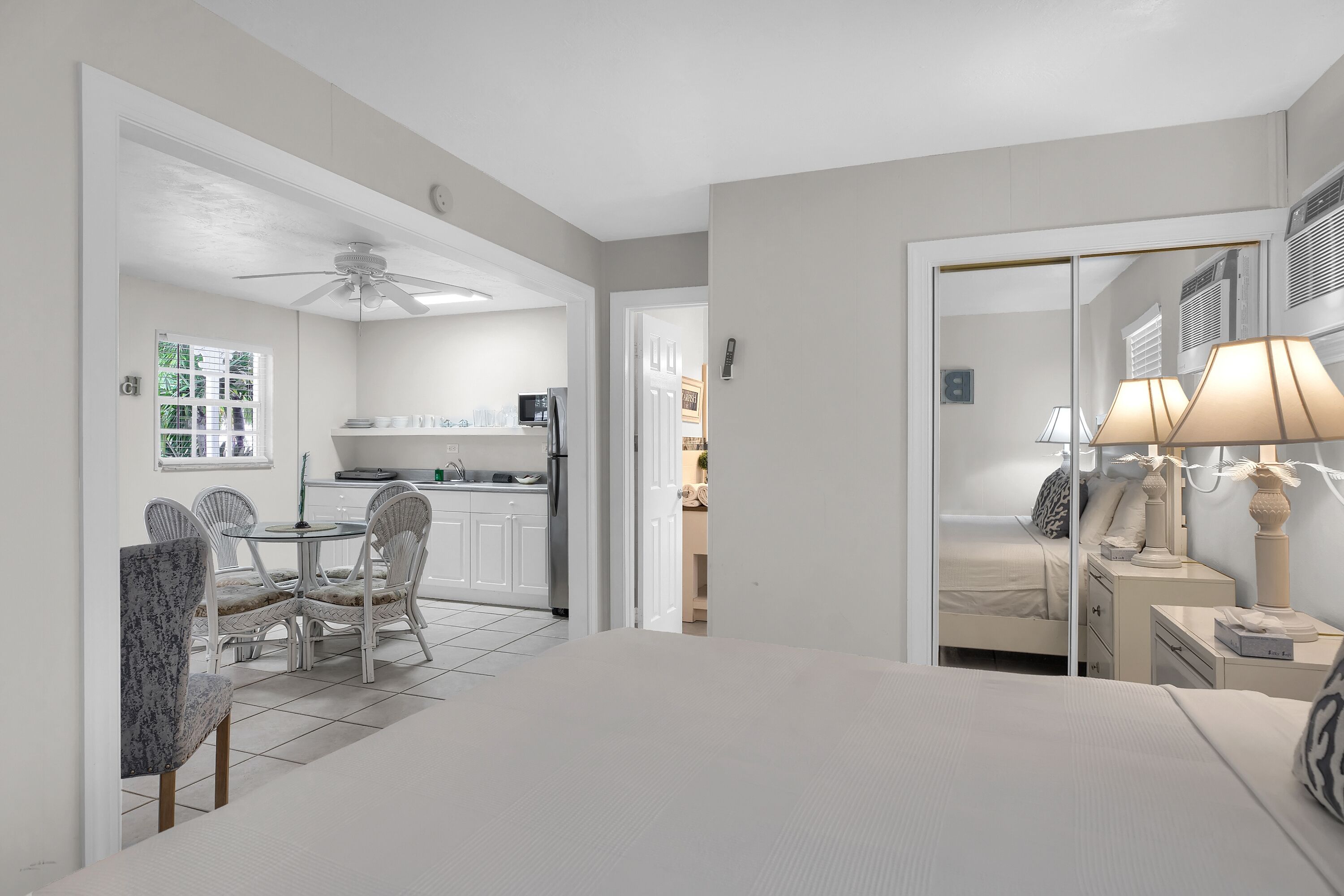 Habitación de hotel moderna con cama, mesita de noche, lámpara y vistas a la cocina y comedor.