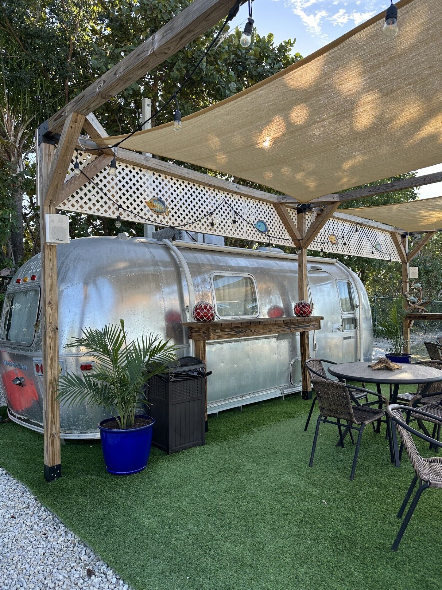 Une vieille caravane dotée d’un patio couvert, d’une table, de chaises et de plantes en pot.