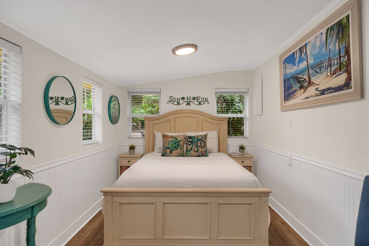 A bedroom with a bed, two nightstands, a potted plant, and a painting on the wall.