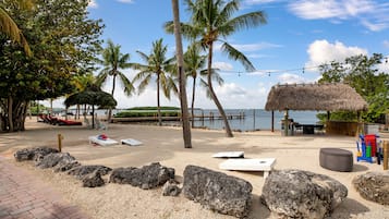 Relax in a serene beach setting with a thatched-roof hut, palm trees, and comfortable lounge chairs.