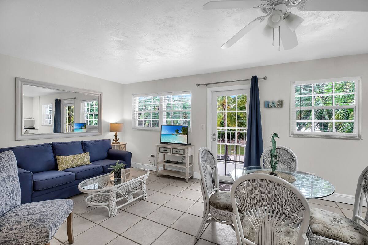 A living room with a blue sofa, wicker chairs, a glass coffee table, and a TV on a white stand.