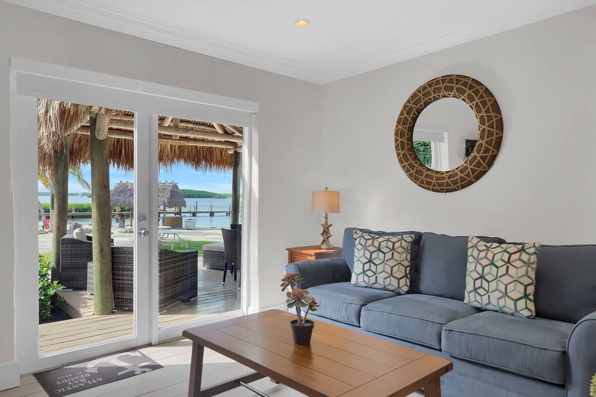A living room with a sofa, a coffee table, and a view of an outdoor deck with a thatched roof.