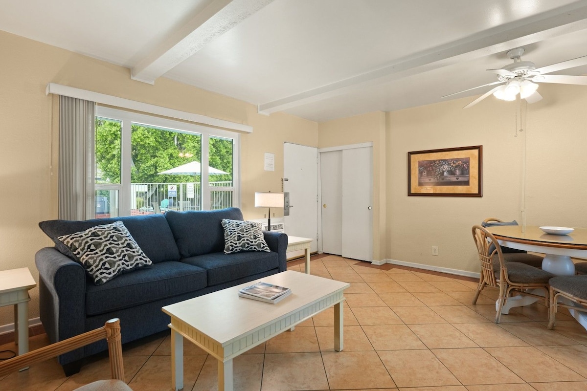 A living room with a sofa, coffee table, dining table, chairs, and a ceiling fan.