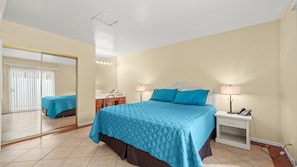 A bedroom with a bed, bedside lamps, a nightstand, a mirror, and a sliding door leading to a balcony.