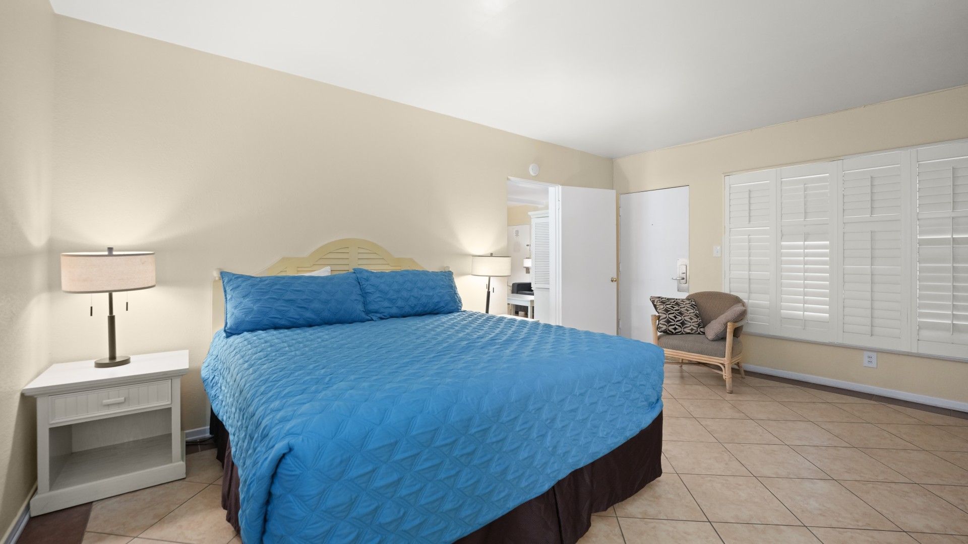 Une chambre à coucher avec un lit, des tables de chevet, une chaise et une fenêtre avec des volets.