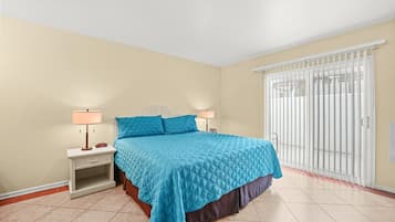 A bedroom with a bed, nightstands, lamps, and a sliding glass door to a balcony.