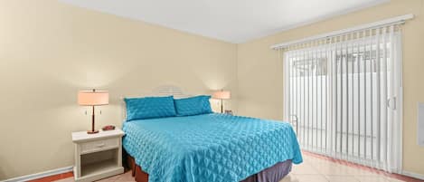 A bedroom with a bed, nightstands, lamps, and a sliding glass door to a balcony.
