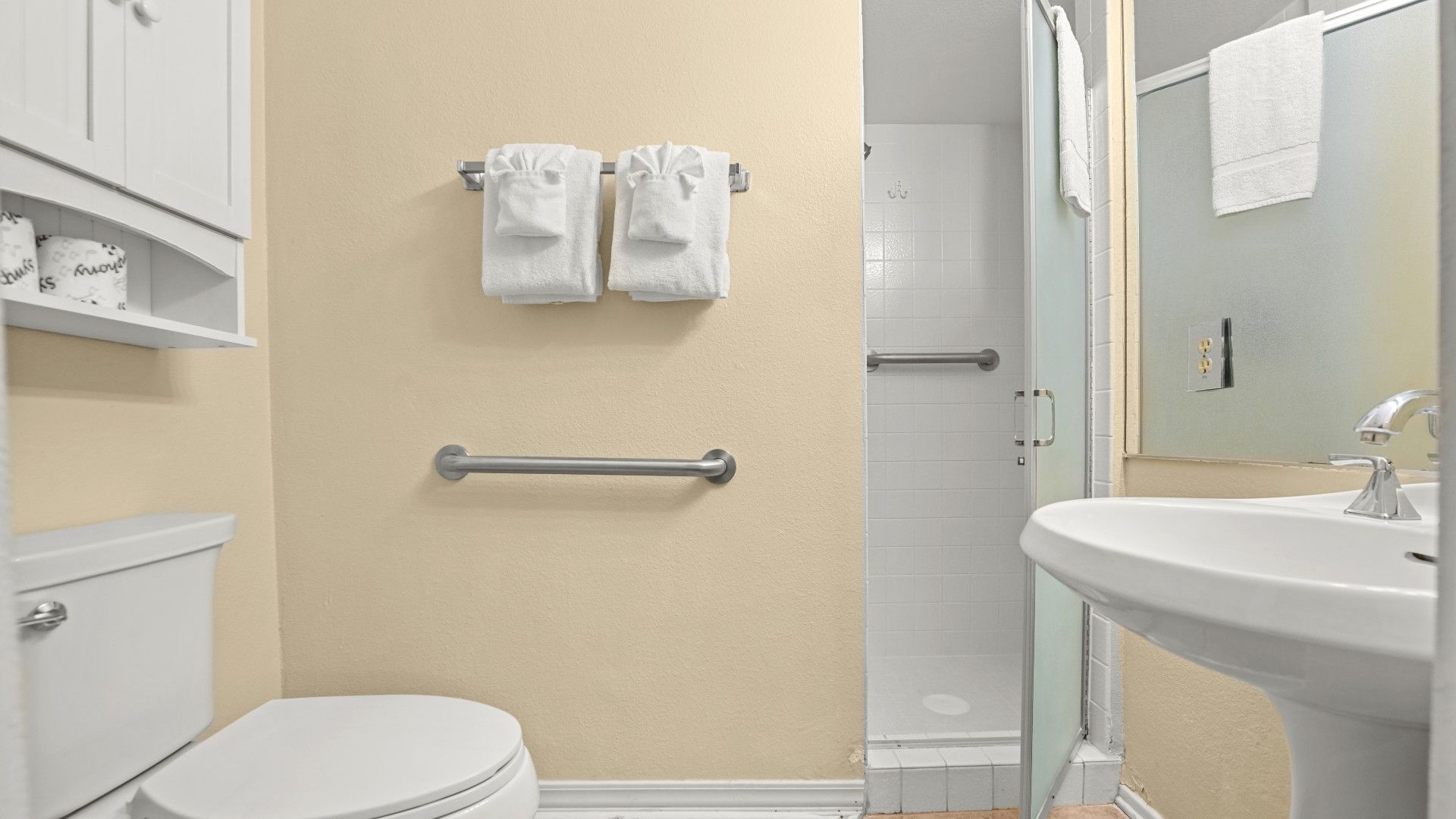 Un bagno con servizi igienici, lavandino e zona doccia. Due asciugamani sono appesi a un porta-asciugamani, c'è una sbarra di sostegno e uno specchio.