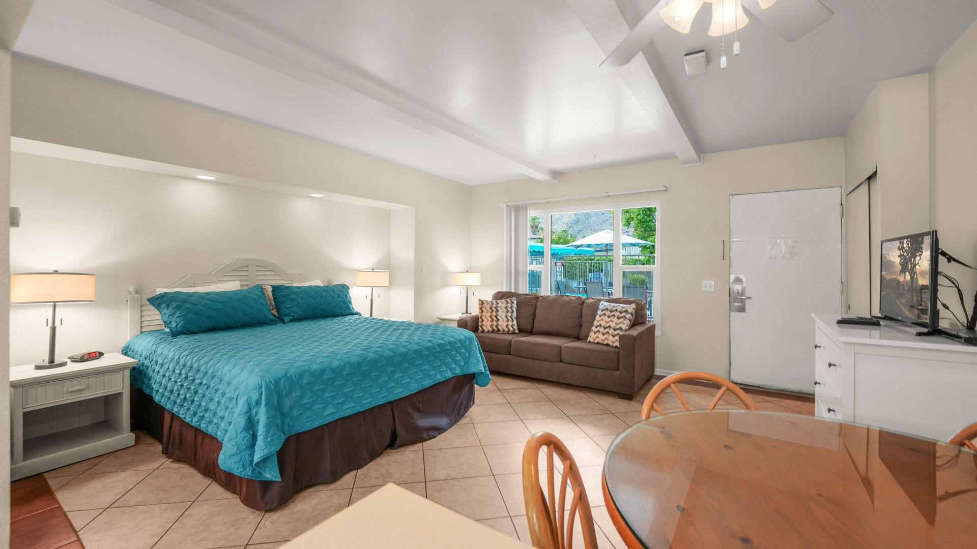 A bedroom with a bed, bedside tables, a sofa, a dining table, and a TV.
