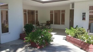 Ein überdachter Patio-Bereich mit Tisch und Stühlen, umgeben von Topfpflanzen und einer Backsteinmauer.