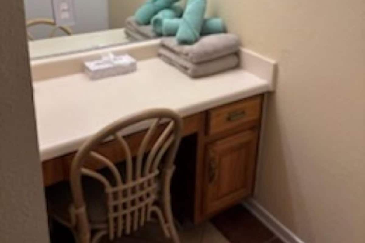 Une petite salle de bain avec un comptoir blanc, une chaise en bois et un miroir.