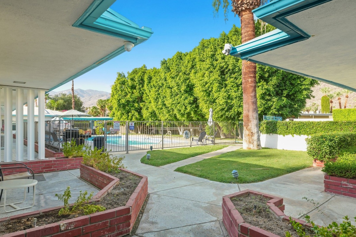 A residential backyard with a swimming pool, a patio area with a table and chairs, and a well-maintained lawn.