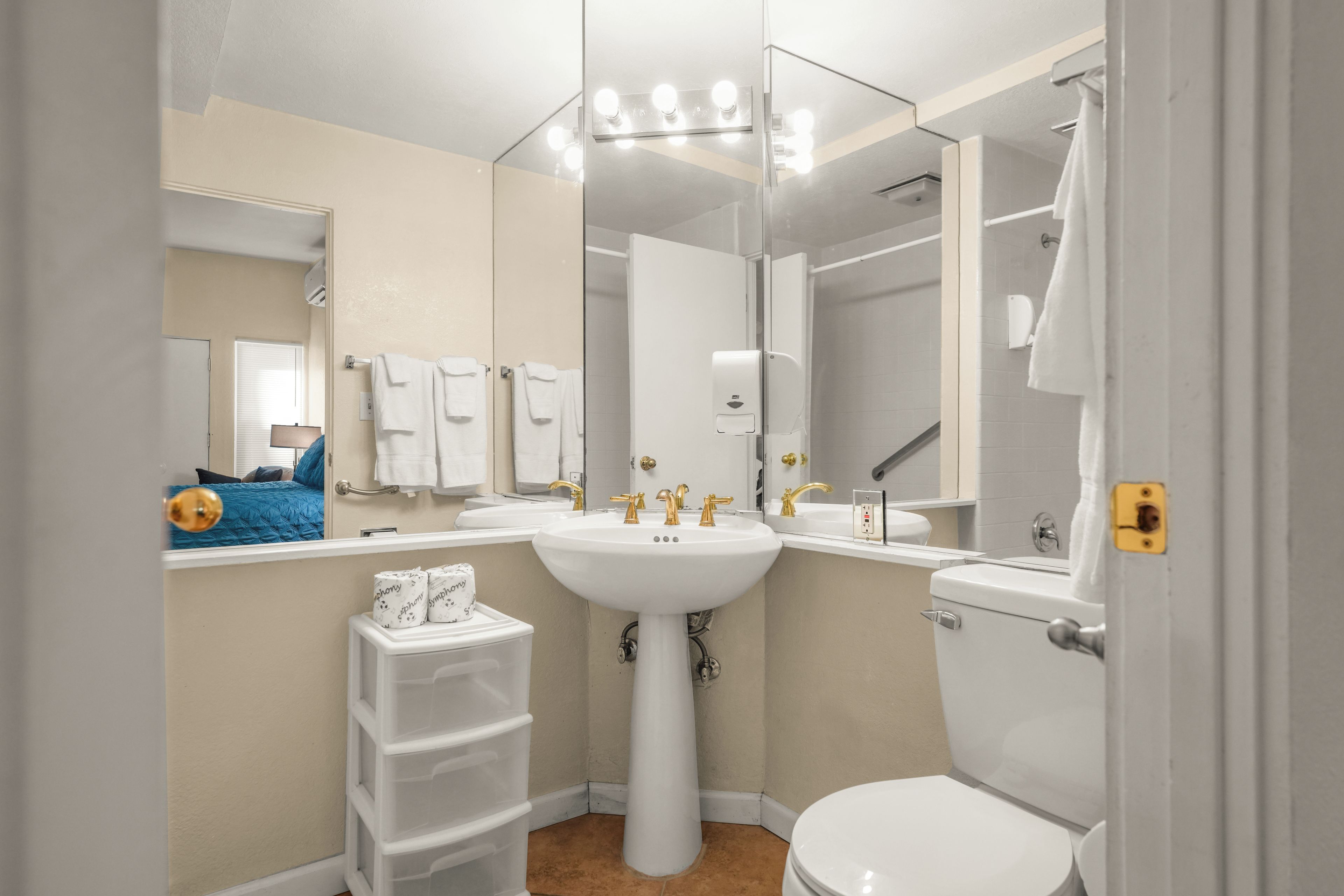 A bathroom with a white sink, gold faucets, a toilet, and a mirror.
