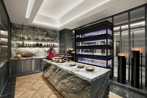 A modern kitchen with marble countertops, a central island, and built-in shelving with kitchenware. - InterContinental Saigon, an IHG Hotel (Ho Chi Minh City)
