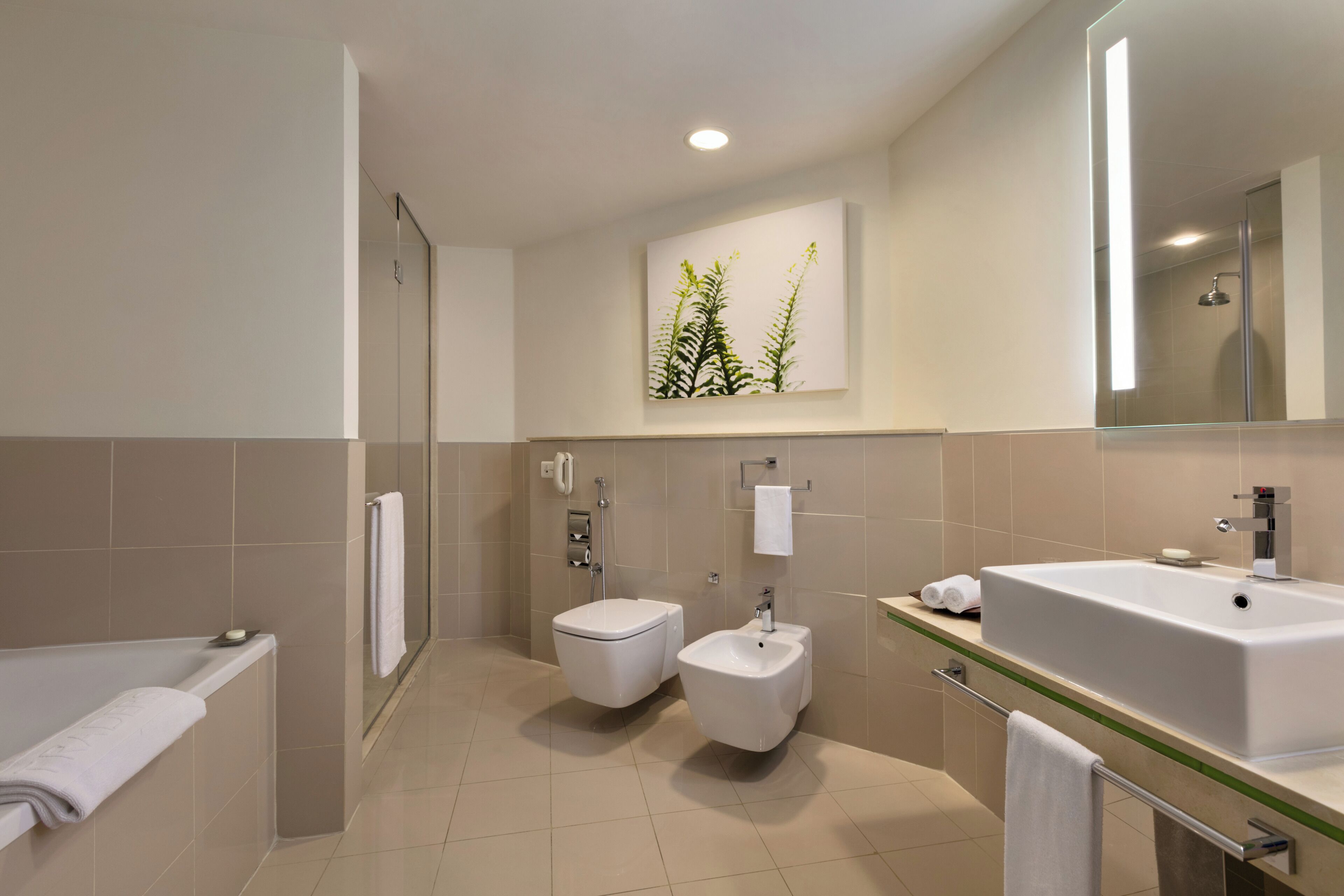 A modern bathroom with a bathtub, two toilets, a bidet, a large sink, and a mirror.