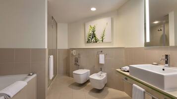A modern bathroom with a bathtub, two toilets, a bidet, a large sink, and a mirror.