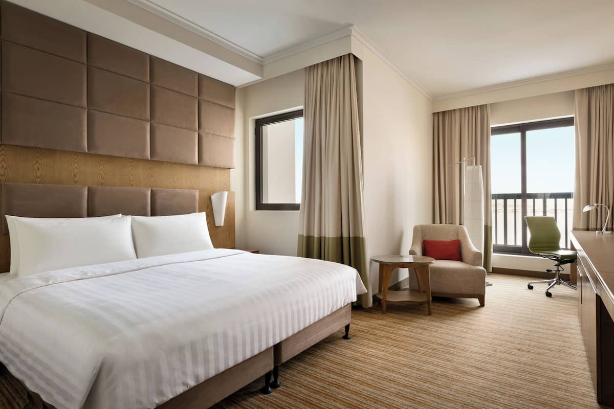 A hotel room with a large bed, a desk, a chair, and a view of the outdoors.