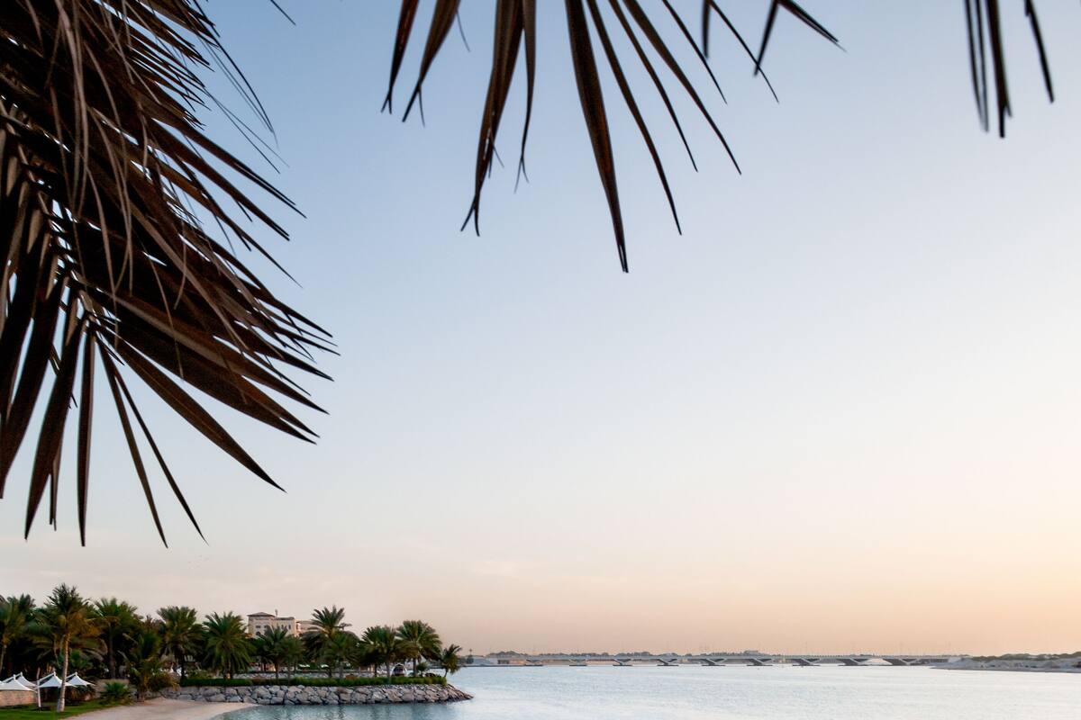 A beach with clear water, a person walking, and palm trees.