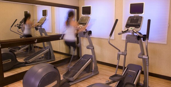Un gimnasio con cintas de correr, elípticas y un espejo grande.