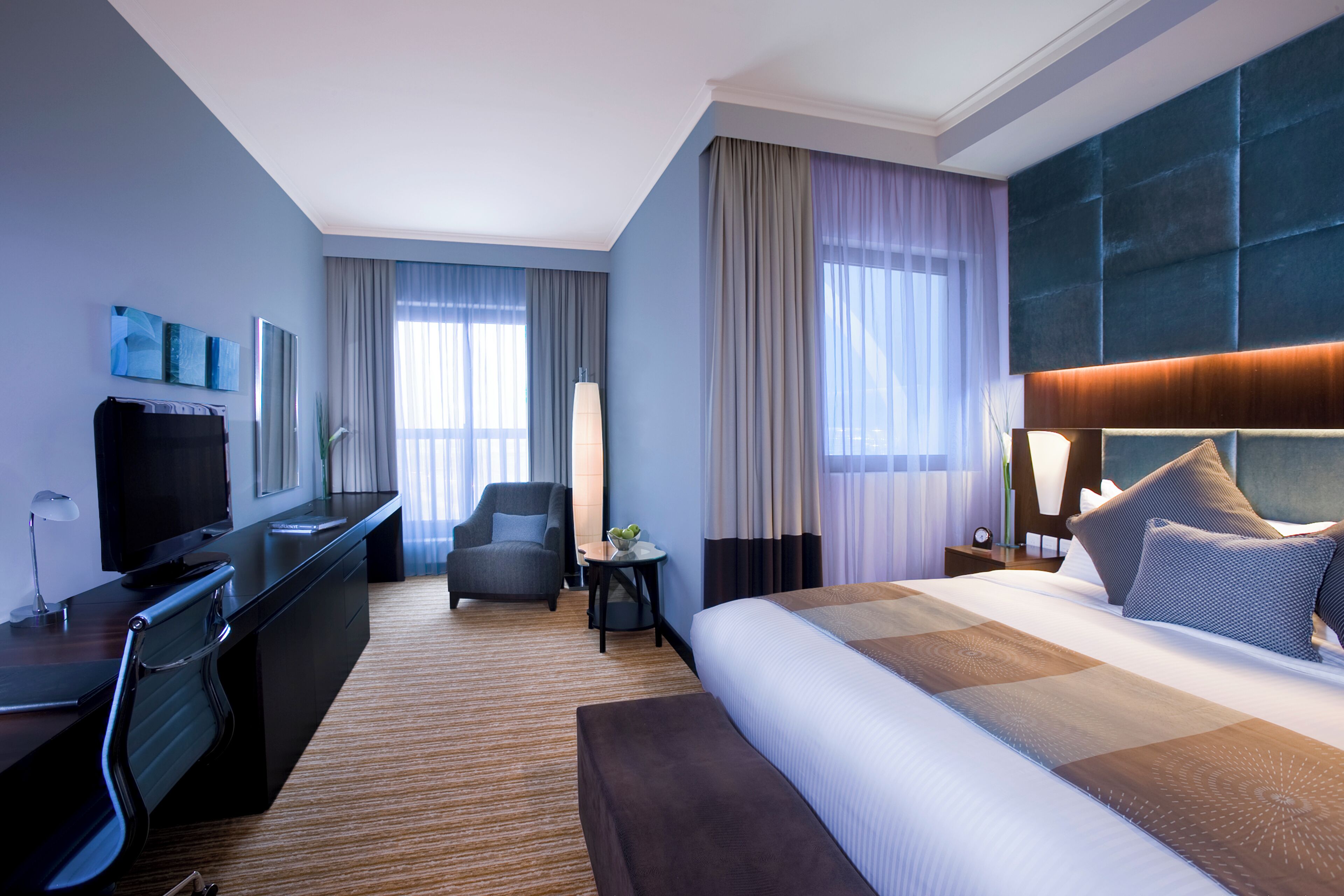 A hotel room with a large bed, a desk with a computer, a chair, and a TV.