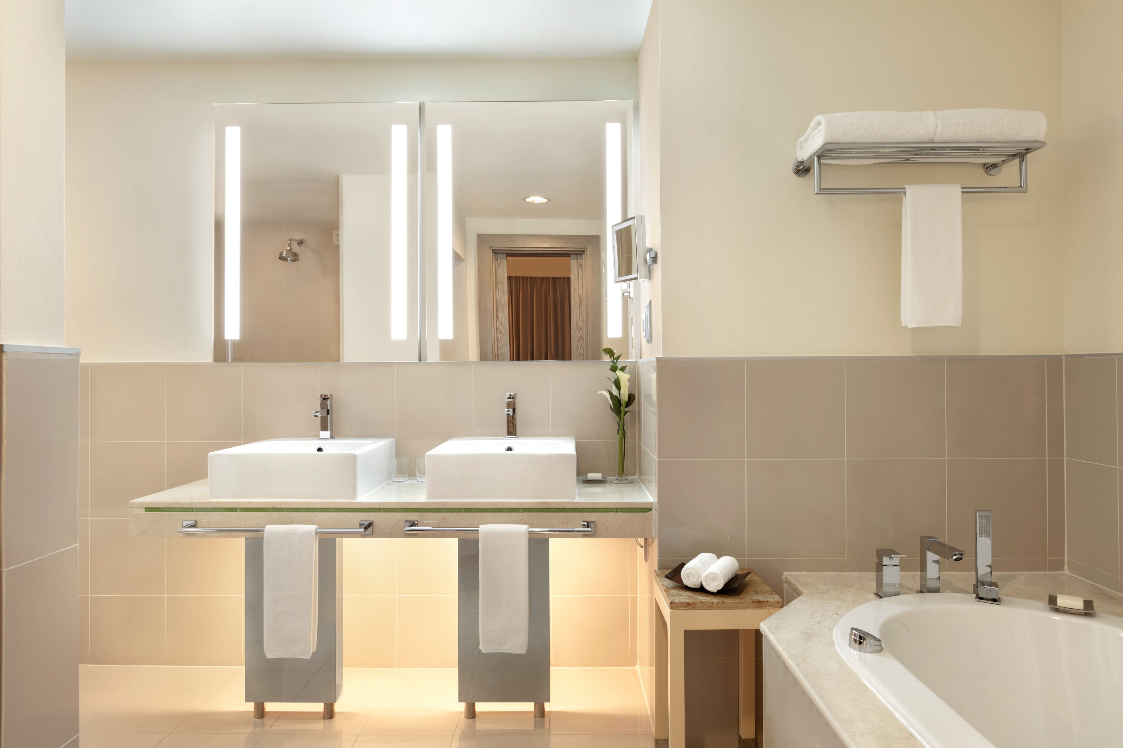 A modern bathroom with two sinks, a large mirror, a towel rack, and a bathtub.
