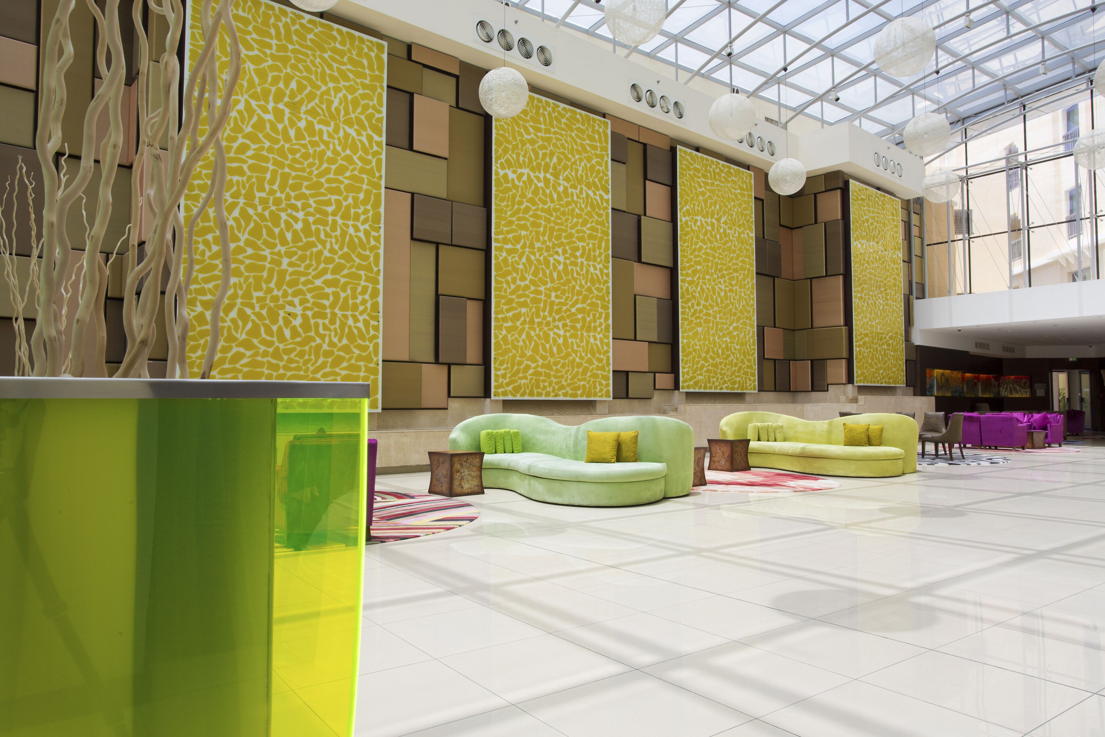 Un hall d’entrée spacieux, aménagé avec un mobilier moderne, notamment des canapés verts et un grand pot de fleurs vert.
