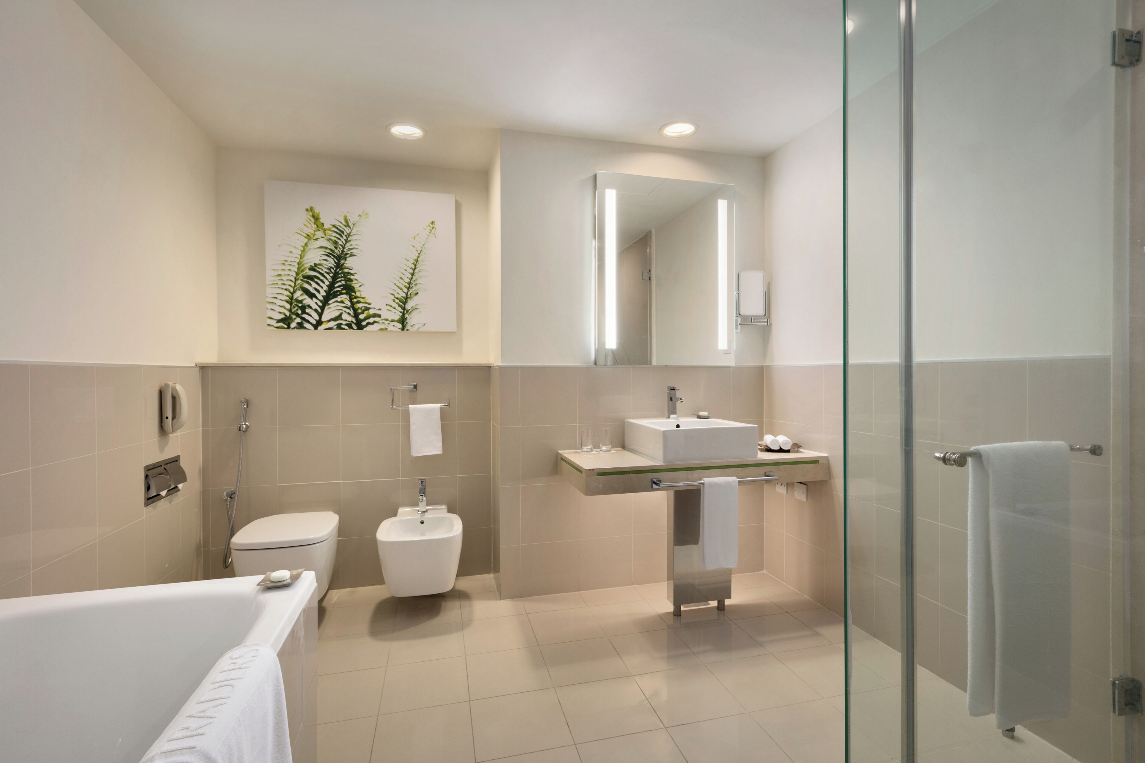 Een moderne badkamer met een bad, toilet, bidet en een douchecabine met glazen wanden.