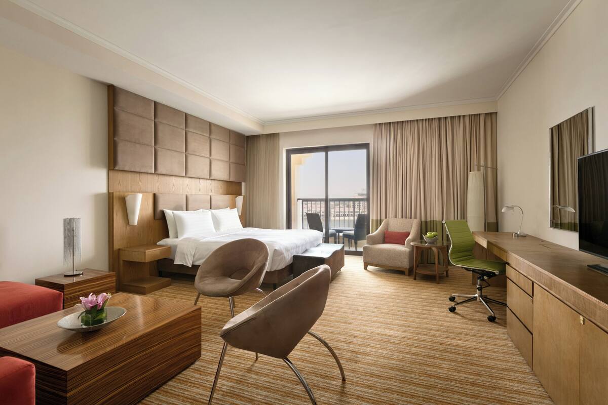 A hotel room with a bed, a desk, a chair, a sofa, and a TV.