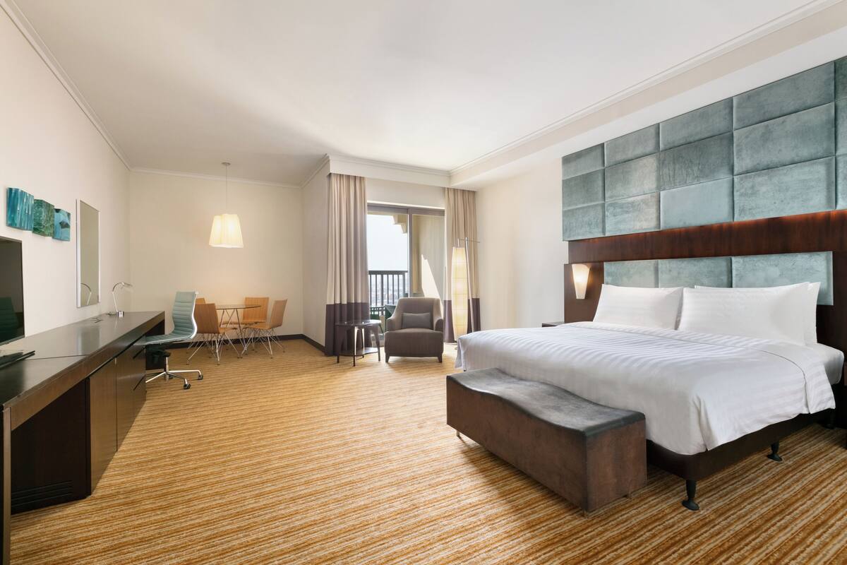 A hotel room with a large bed, a desk, a chair, and a small table.