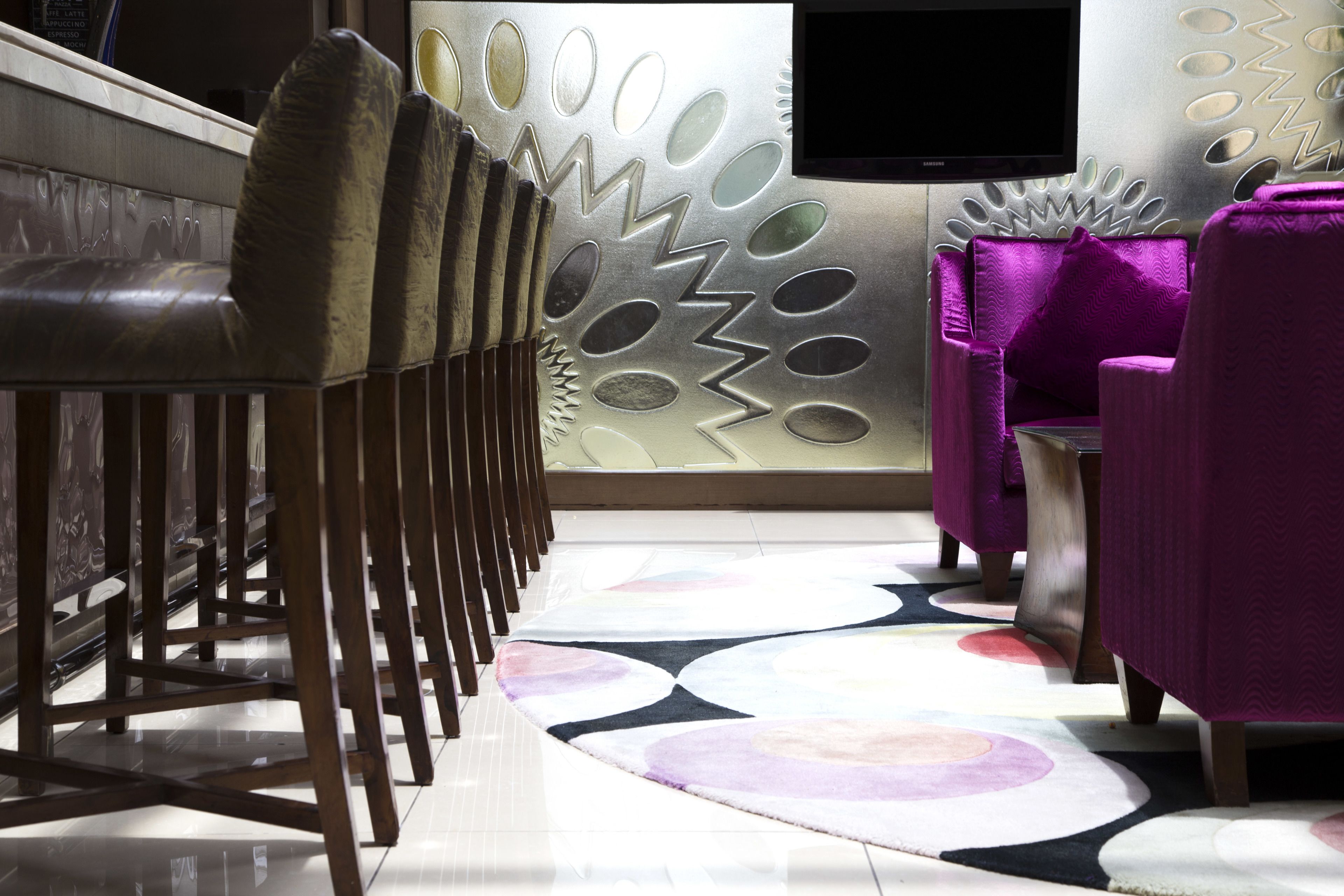 Zona de bar con una fila de sillones de cuero, un tapiz estampado y una pared con diseño geométrico.