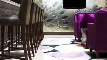 Zona de bar con una fila de sillones de cuero, un tapiz estampado y una pared con diseño geométrico.