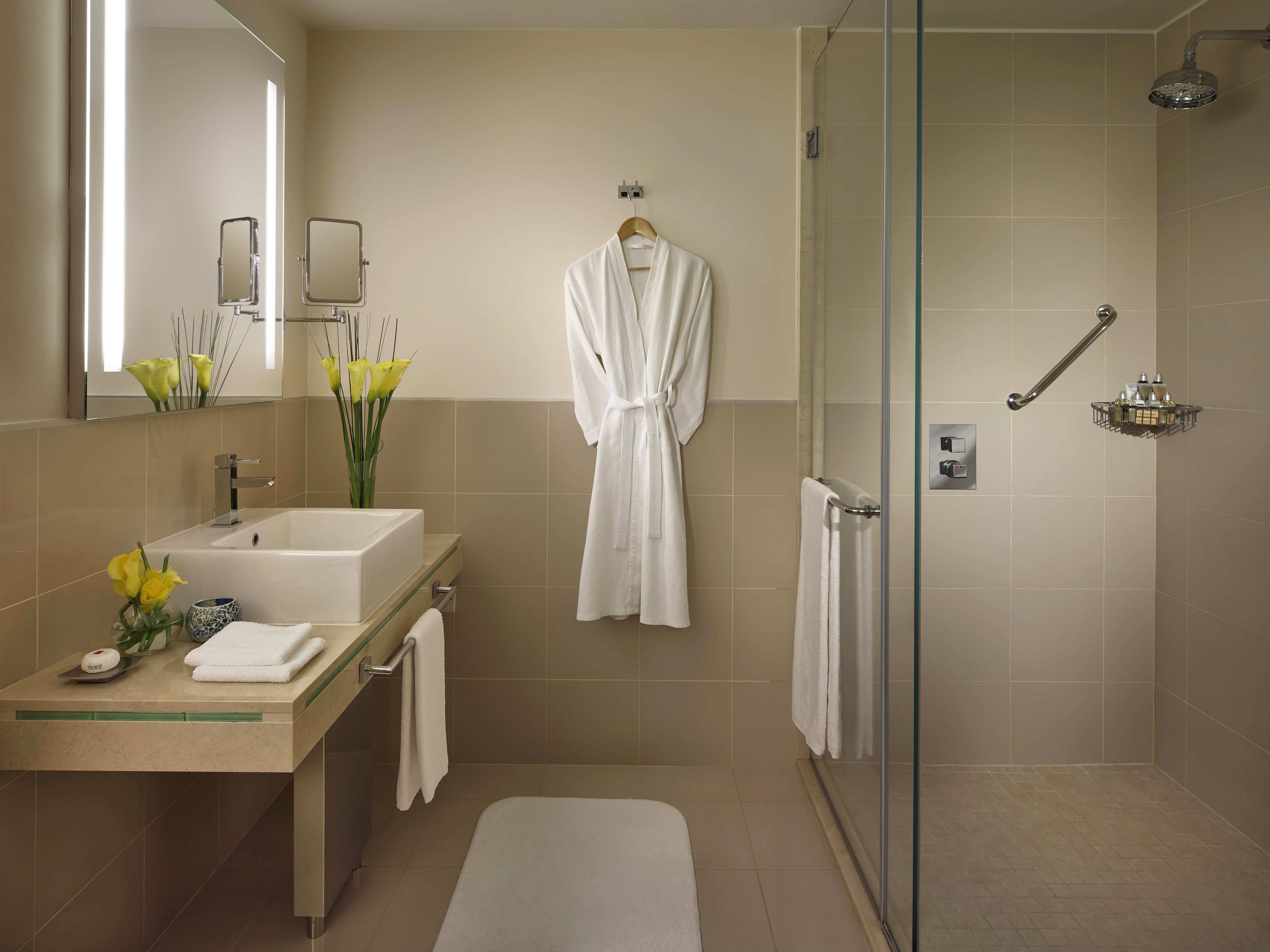 A modern bathroom with a glass-enclosed shower, a vanity with a sink and mirror, and a robe hanging on the wall.