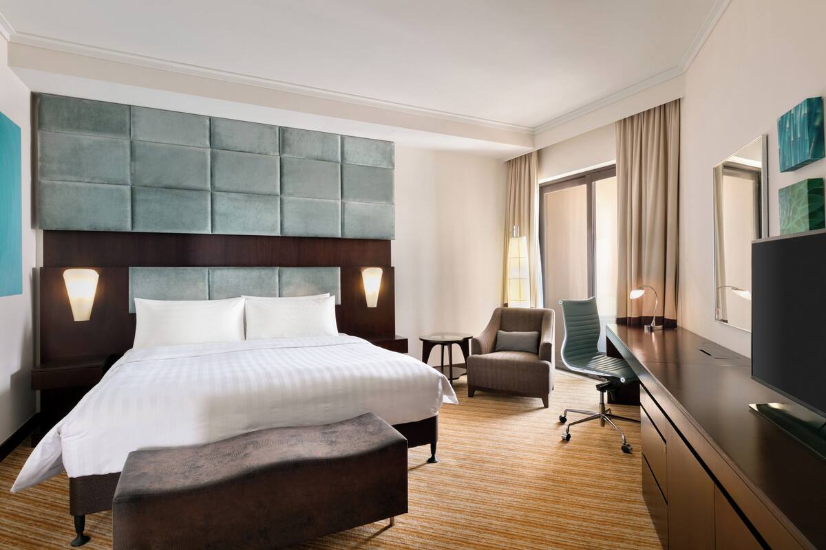 A hotel room with a large bed, a desk, a chair, and a television.