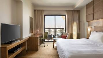Ein Hotelzimmer mit einem Bett, einem Fernseher auf einem Holzboden, einem Schreibtisch, einem Stuhl und Blick auf die Stadt durch große Fenster.