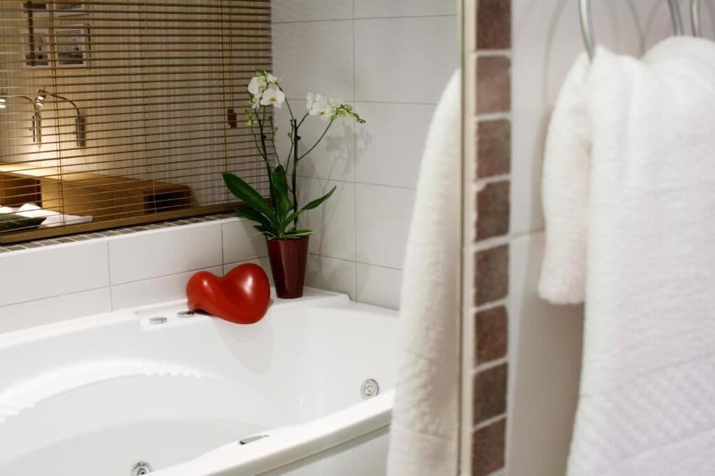 Un bagno moderno con una vasca da bagno bianca, una pianta in vaso e un oggetto a forma di cuore rosso sul bordo.