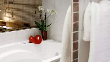 Un bagno moderno con una vasca da bagno bianca, una pianta in vaso e un oggetto a forma di cuore rosso sul bordo.