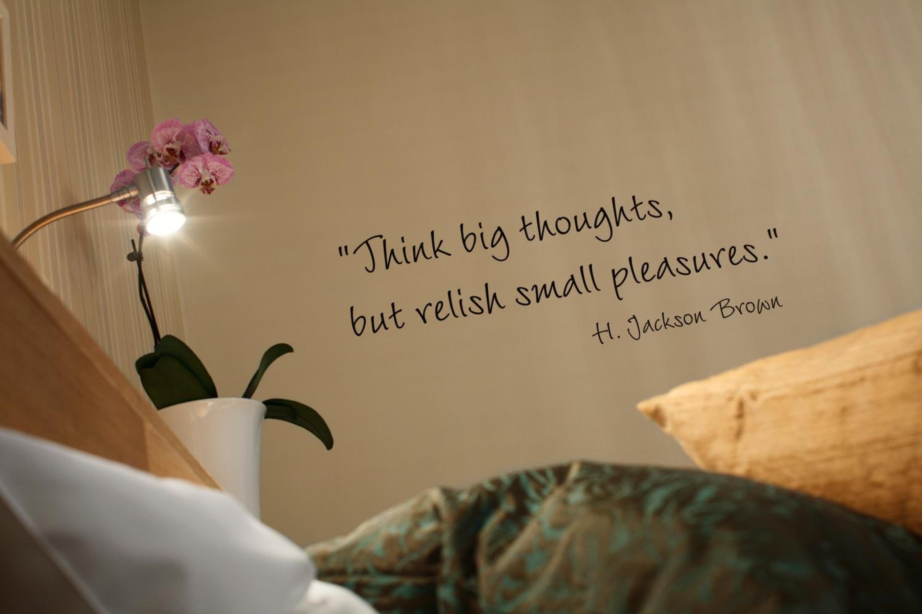 A wall with a quote by H. Jackson Brown, a bedside lamp, and a potted orchid.