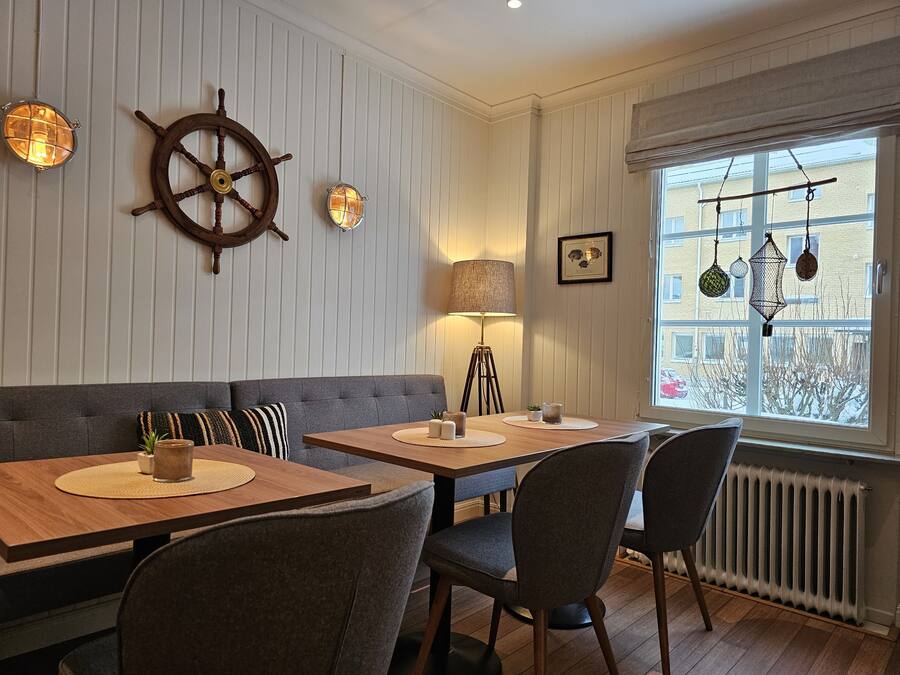 Un coin repas avec une table et des chaises en bois, un canapé gris et une décoration murale représentant un gouvernail de bateau.