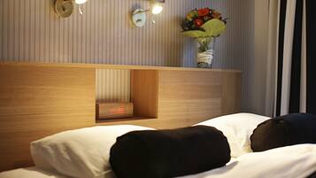 Una habitación de hotel con cabecera de madera, una mesita de noche con un reloj y un florero sobre la mesita.