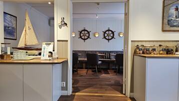 Una cocina moderna con suelo de madera, un comedor con mesa y sillas blancas, y decoración temática náutica que incluye una maqueta de un velero y timones de barco.