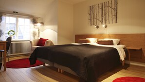 A bedroom with a large bed, a wooden headboard, a red rug, a desk with a chair, and a window with a wreath.