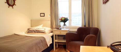 A bedroom with a bed, a desk, a chair, a red rug, and a window with curtains.