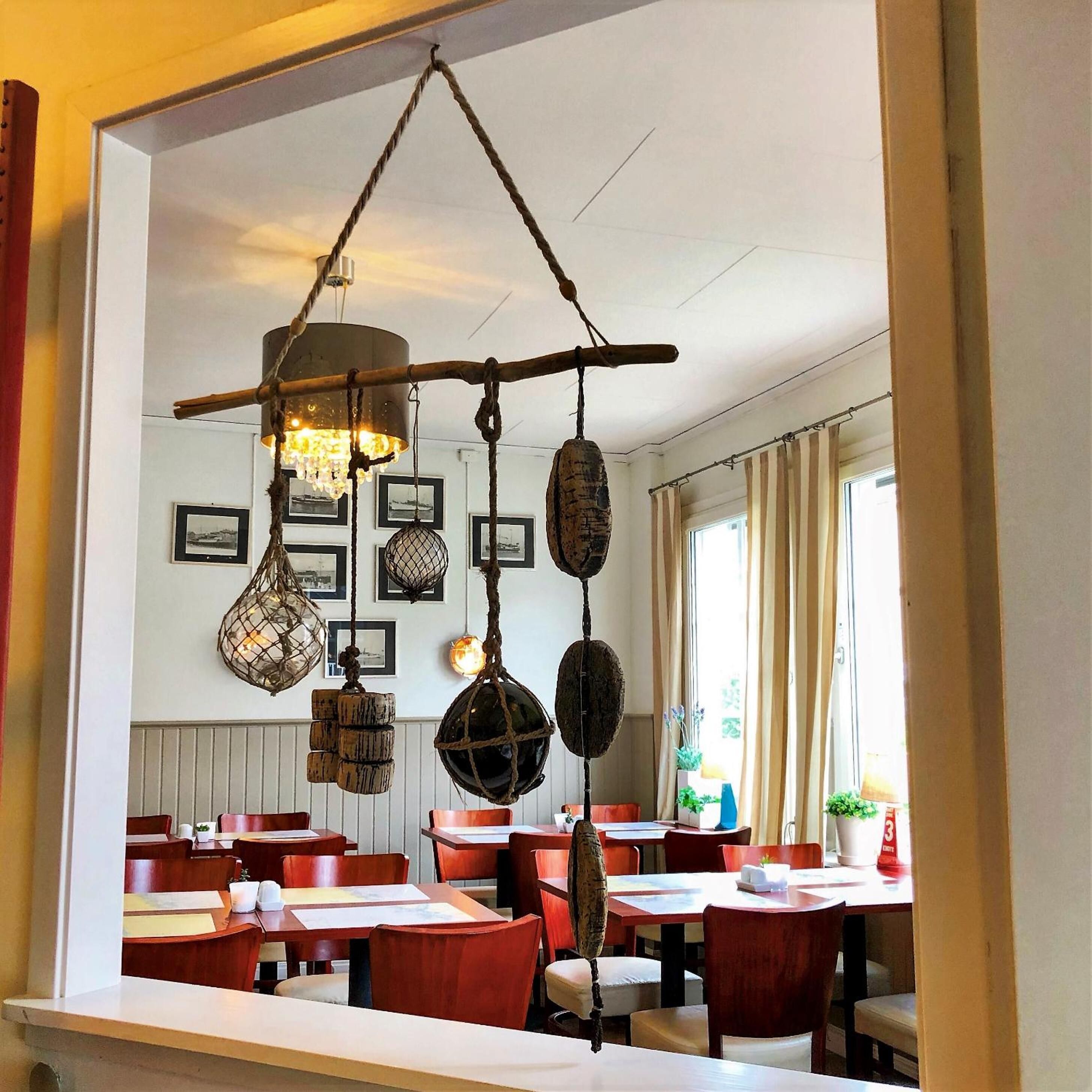 Interno di un ristorante con tavoli e sedie in legno, decorazioni appese e quadri alle pareti.