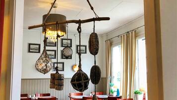 Interno di un ristorante con tavoli e sedie in legno, decorazioni appese e quadri alle pareti.